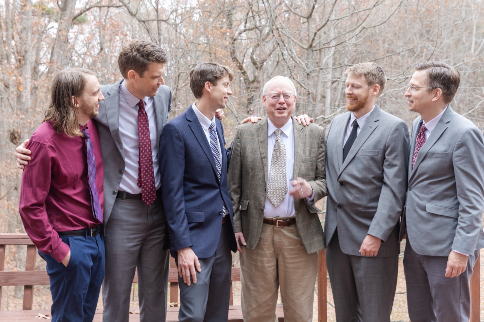 Hans Andersen laughing with five of his grown sons, all in suits, standing together on a deck in the autumn woods.